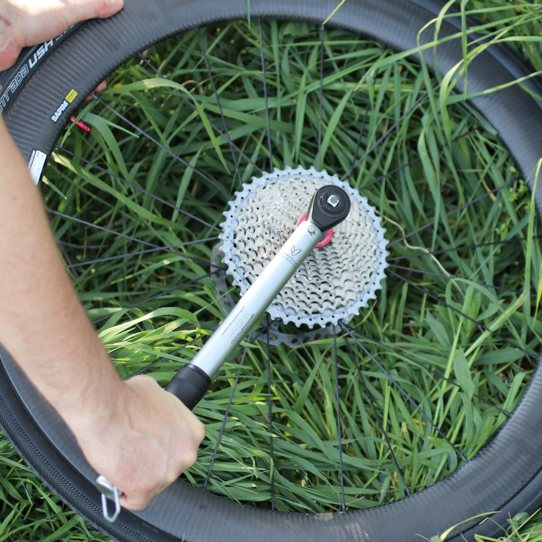 Person using a Giustaforza 1-60 Pro torque wrench on a bicycle wheel with a cassette on grass