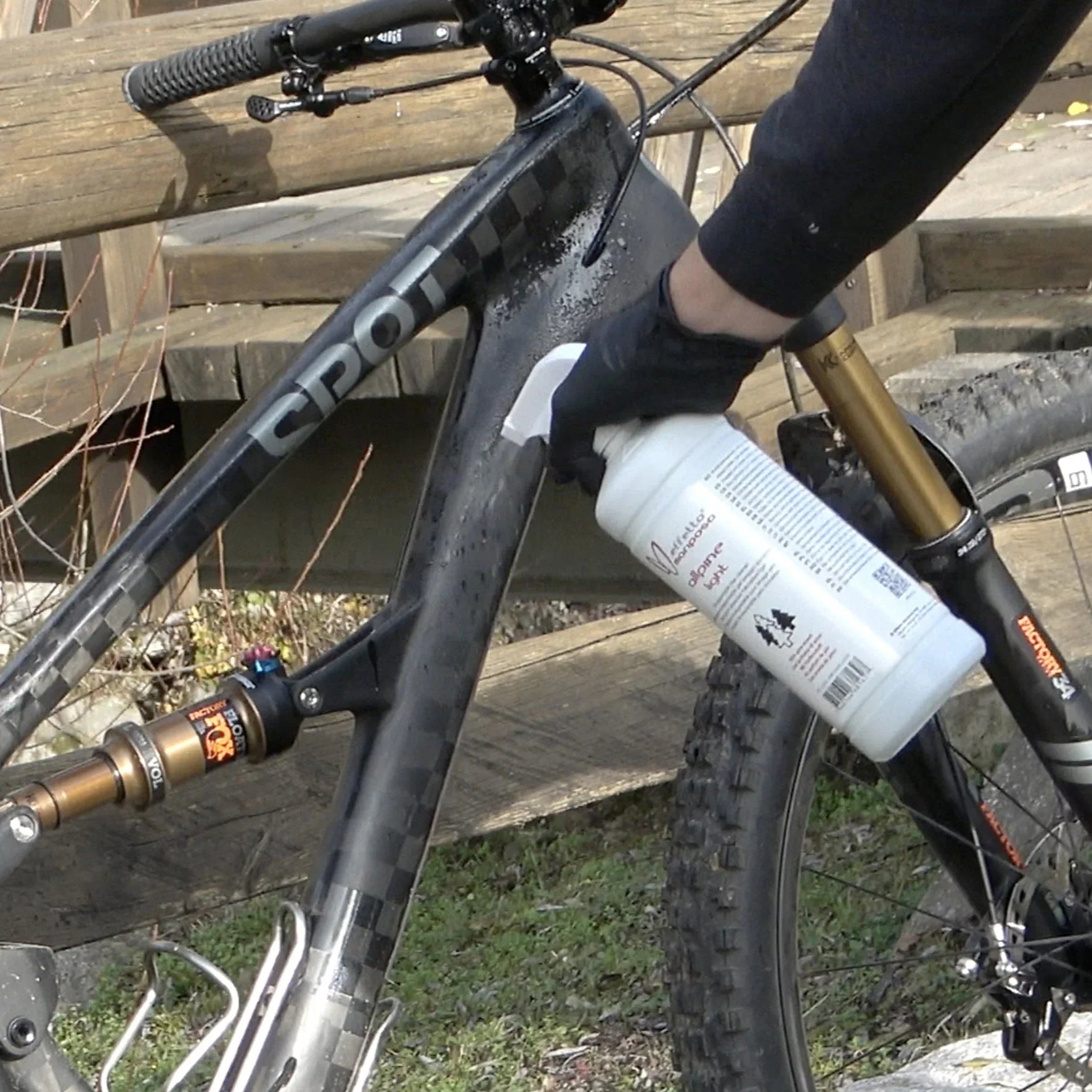Spraying bike cleaner on black mountain bike frame outdoors