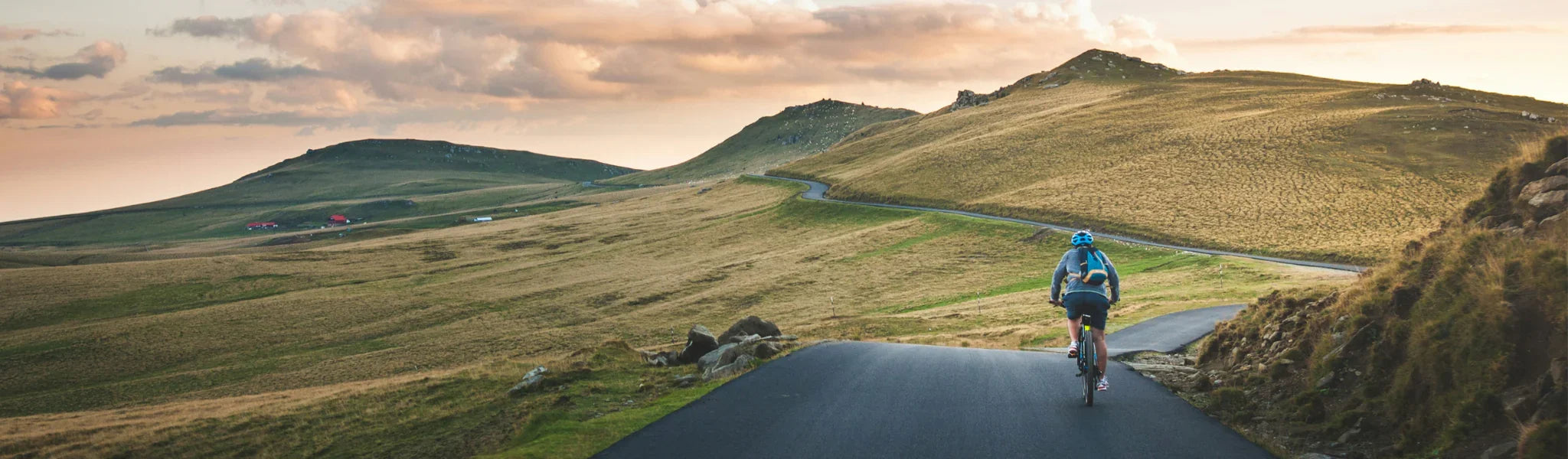 Cyclist riding on winding road through scenic grassy hills at sunset